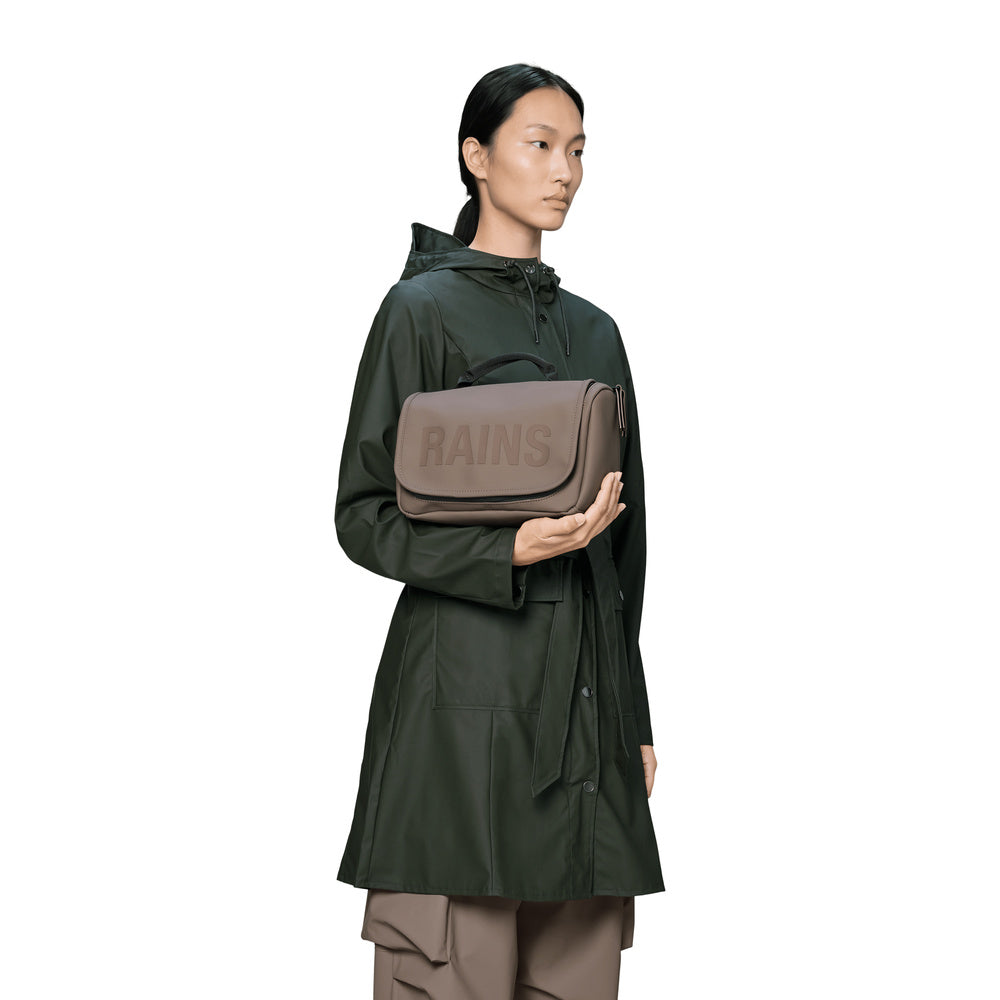 Beauty case Rains Texel Wash Bag Cinder – tenuto in mano da una modella